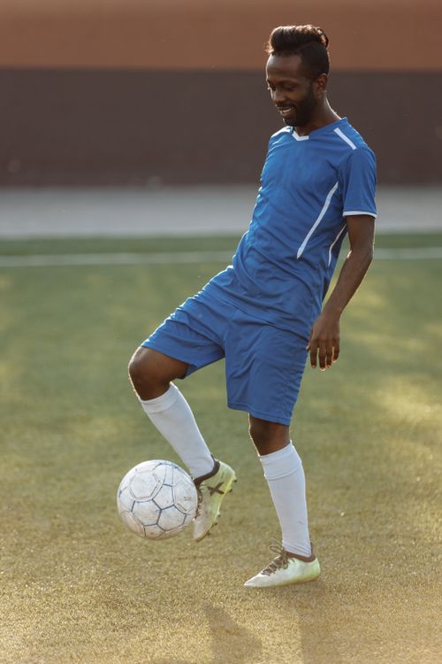 Free African American soccer player practicing on grassy field in blue jersey during daytime. Stock Photo