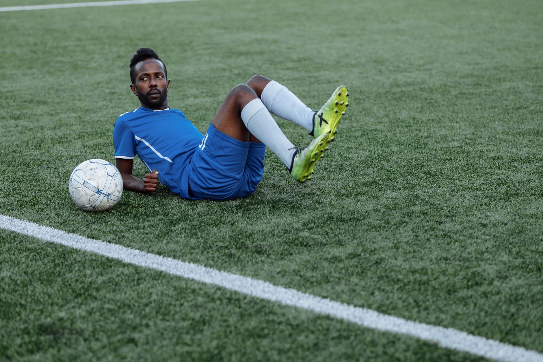 A soccer player in blue jersey lying on the field with a ball beside him.
