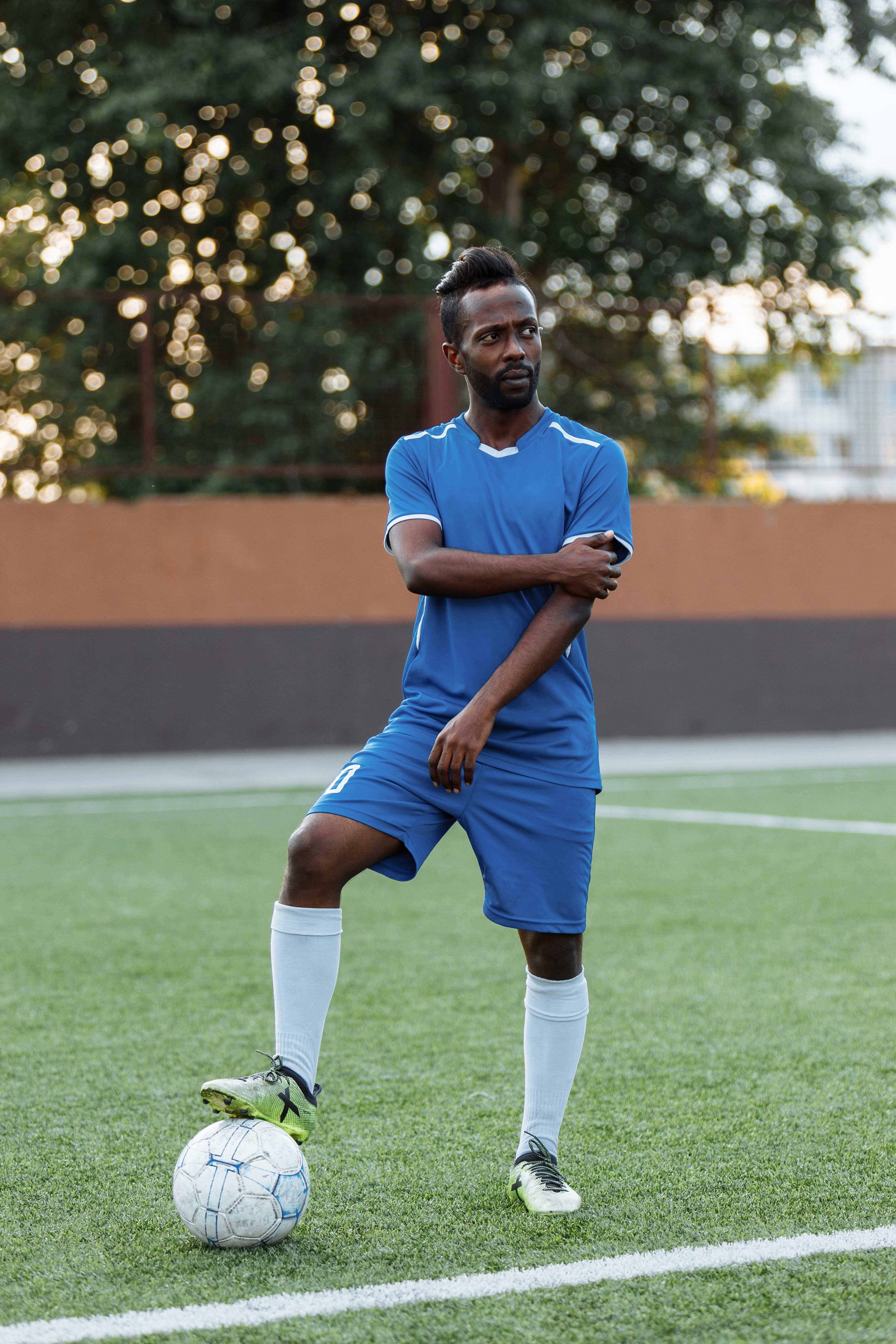 a man in blue shirt and shorts standing on the field while stepping on the ball