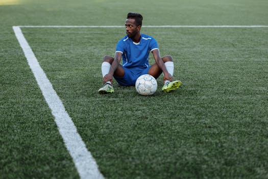 A soccer player in a blue uniform sits on a green field with a ball, reflecting focus and sportsmanship.