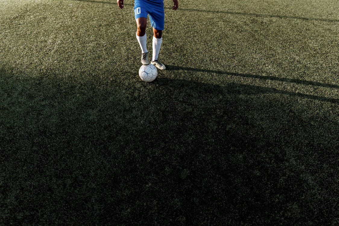 Legs of Football Player with Ball on Grass Field