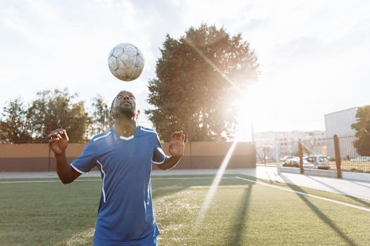 A soccer player skillfully juggles a ball on a sunlit field, showcasing sports and fitness prowess.