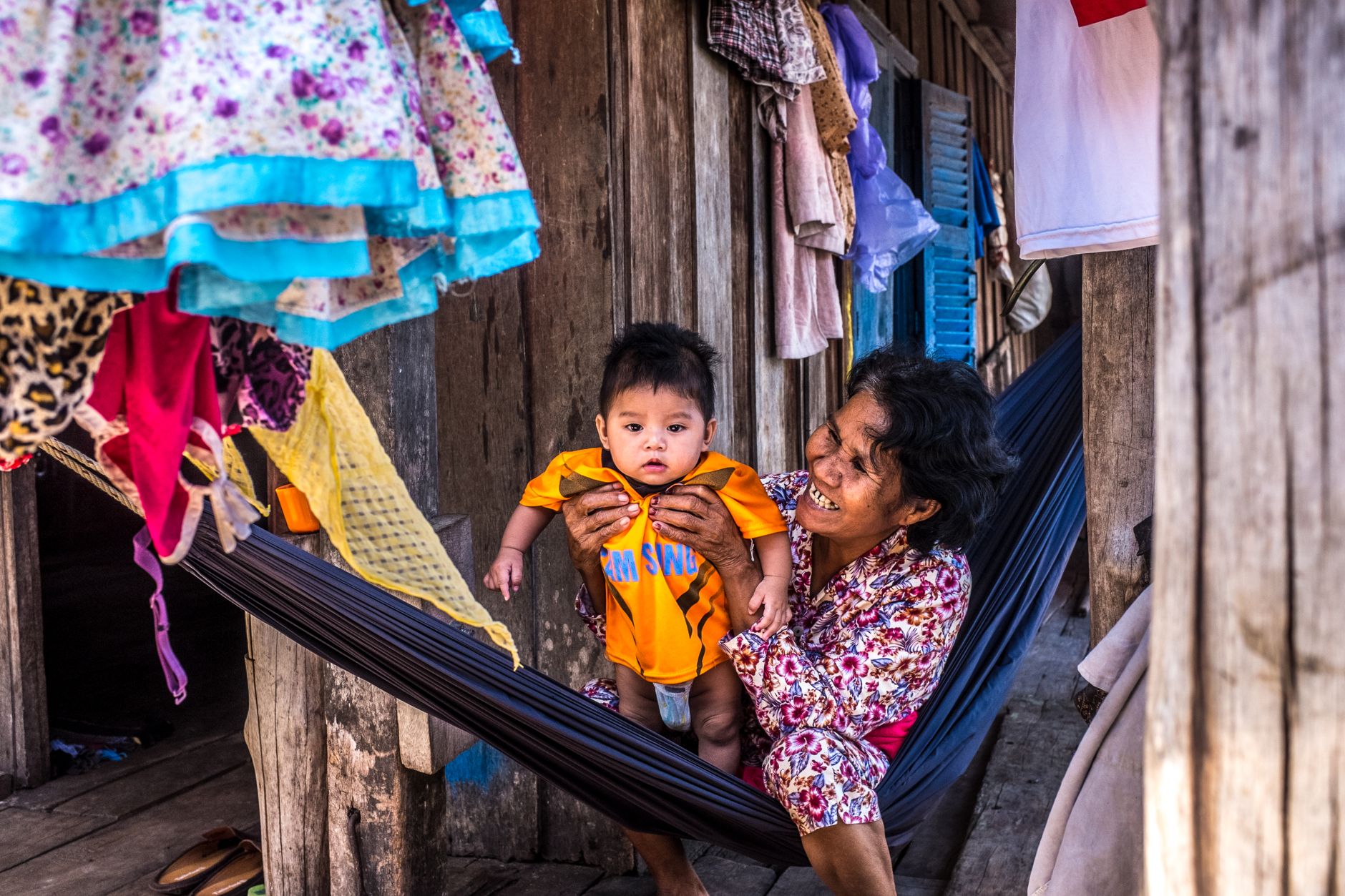 A joyful grandmother holds her grandchild in a hammock, depicting a warm family moment in Cambodia.