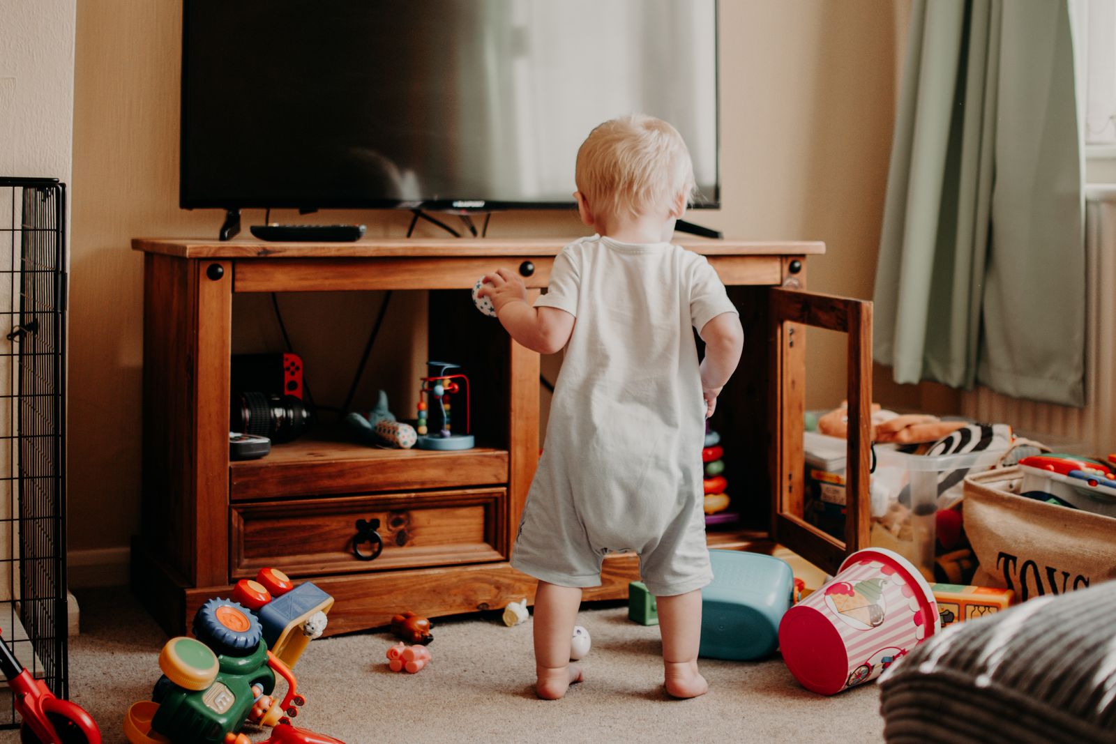 Toddler playing in a toy-filled living room representing the sensory load and household noise that can overwhelm moms