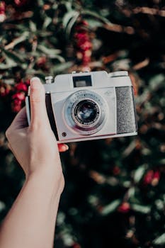 Close-up of a hand holding a vintage camera against a blurred natural background.