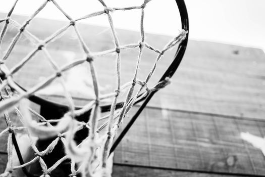 Low angle closeup of black and white basketball hoop hanging in wooden board in sports ground