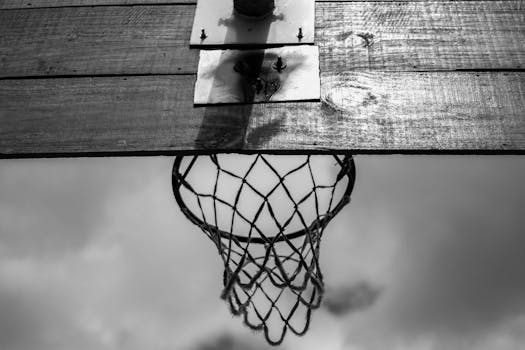 From below of black and white wooden backboard with basketball net hoop hanging against cloudy sky
