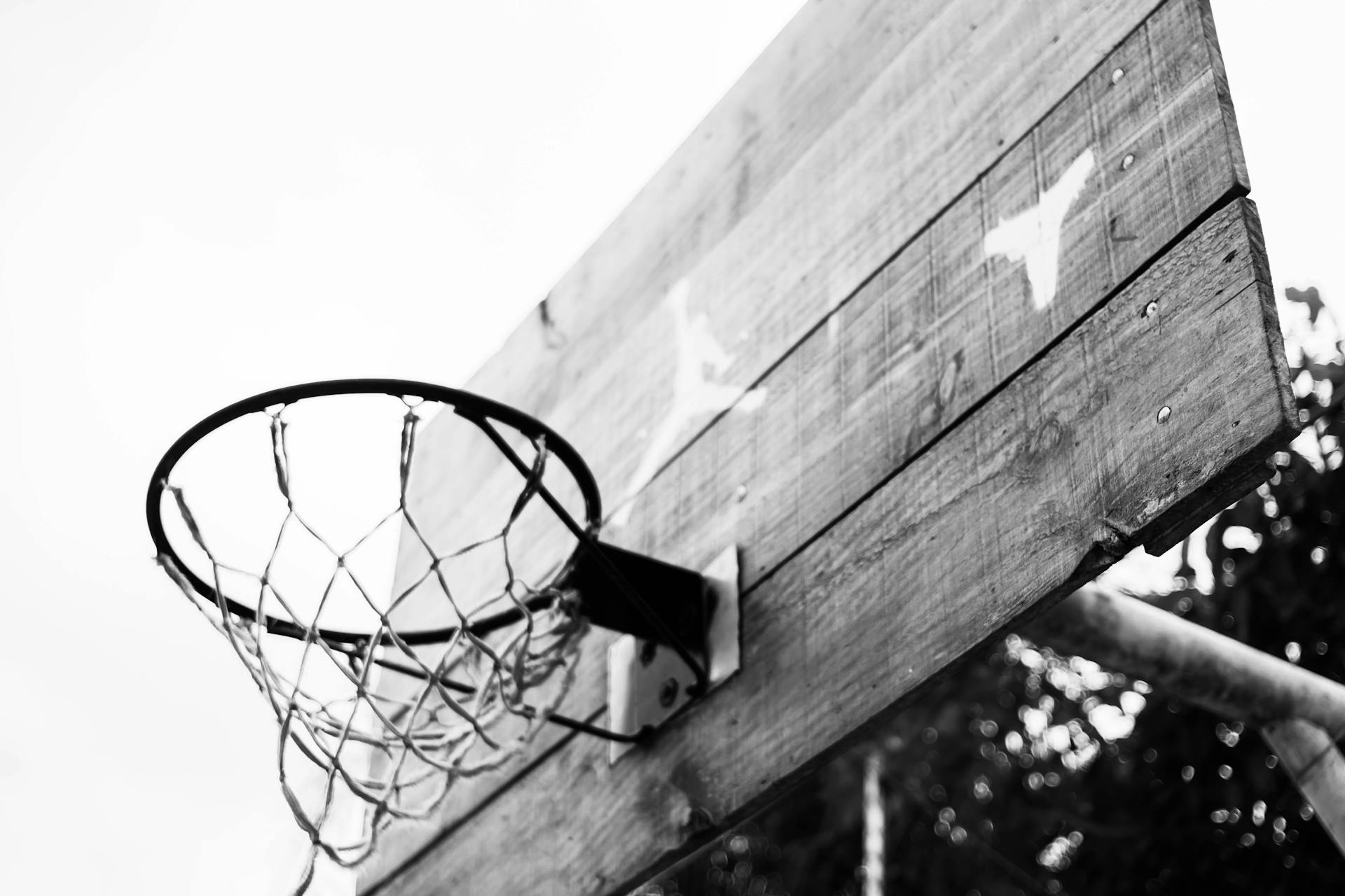 From below of black and white basketball hoop hanging on backboard on sports ground in park