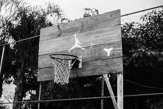 Black and white photo of a rustic wooden basketball hoop on an outdoor court.