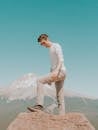 Man in White Long Sleeve Shirt and White Pants Sitting on Brown Wooden Seat Looking at on on on on