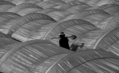 Free Black and white of unrecognizable male farmer with shovel walking between hothouses in countryside Stock Photo