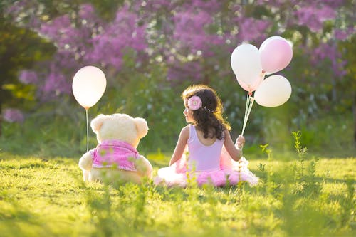 Free Little Girl Sitting with Her Teddy Bear and Holding Balloons  Stock Photo