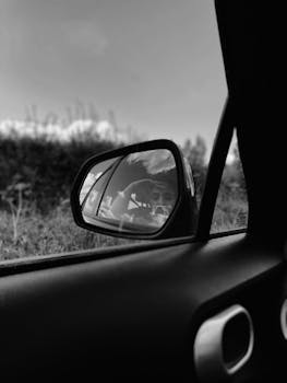 Black and white of thoughtful person reflecting from small wing mirror of automobile in daylight