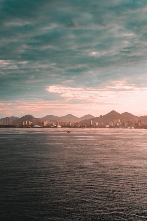 Sea and a Distant City and Mountains at Dusk under Dark Clouds 