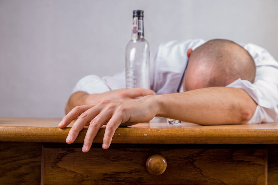 Man in White Dress Shirt Holding Glass Bottle on Brown Wooden Table