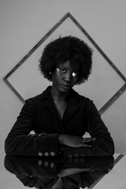 Black and white portrait of a woman with afro hair and artistic facial elements, exuding elegance.