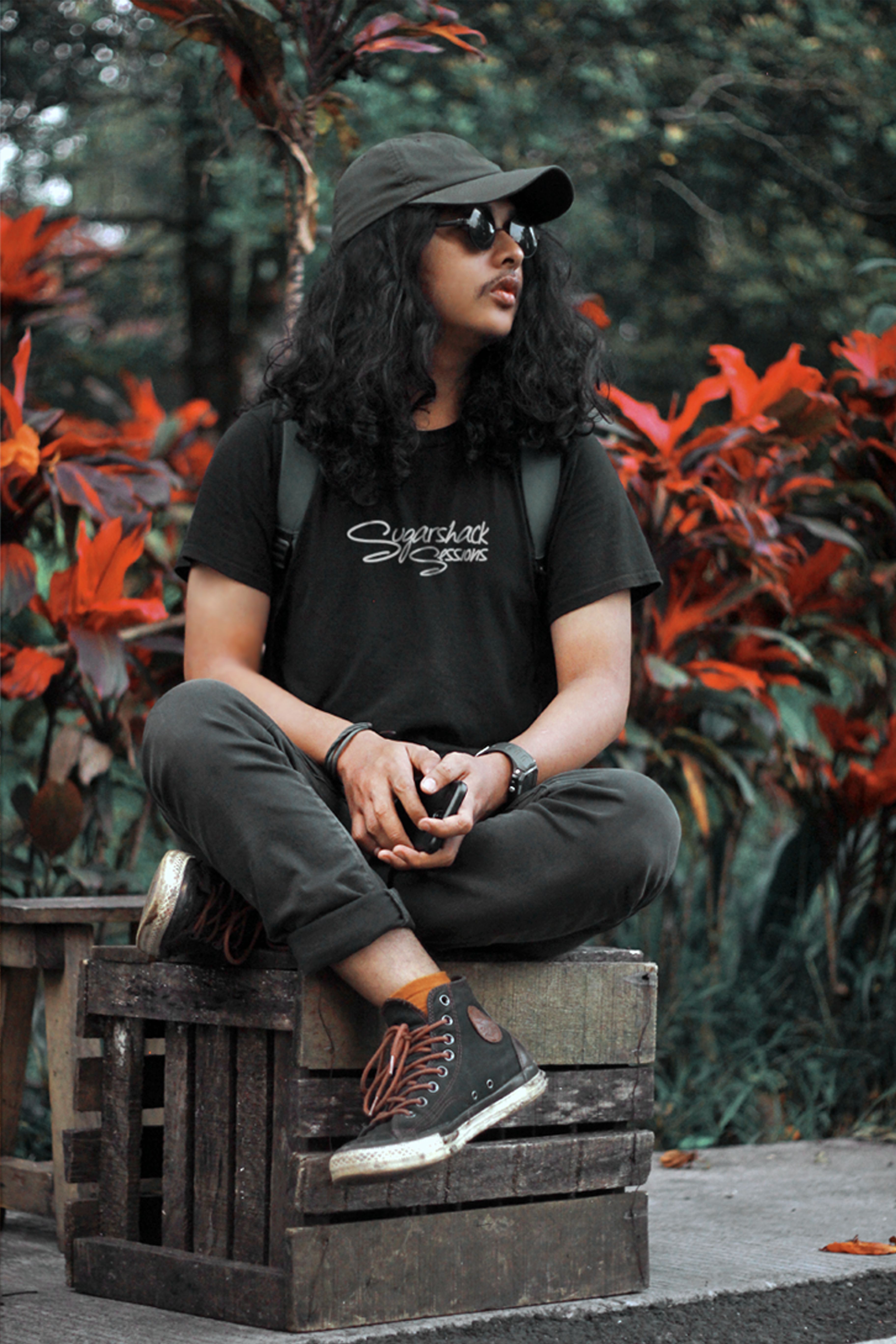 Man in streetwear sitting outdoors, surrounded by lush foliage in South Sulawesi.