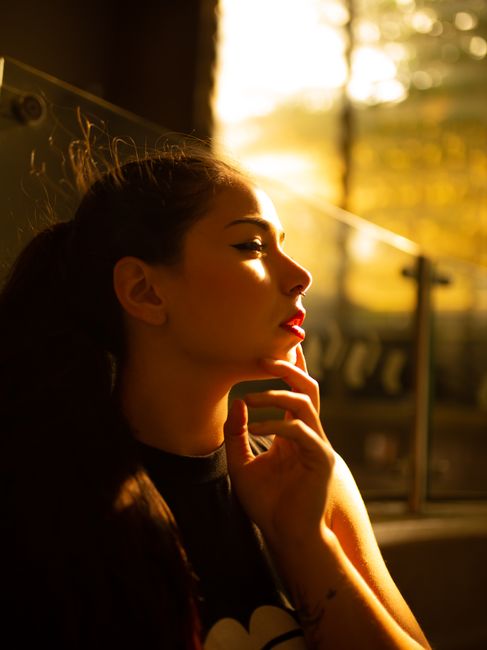 A woman leans against a wall, highlighted by warm golden sunlight, creating a dramatic silhouette.