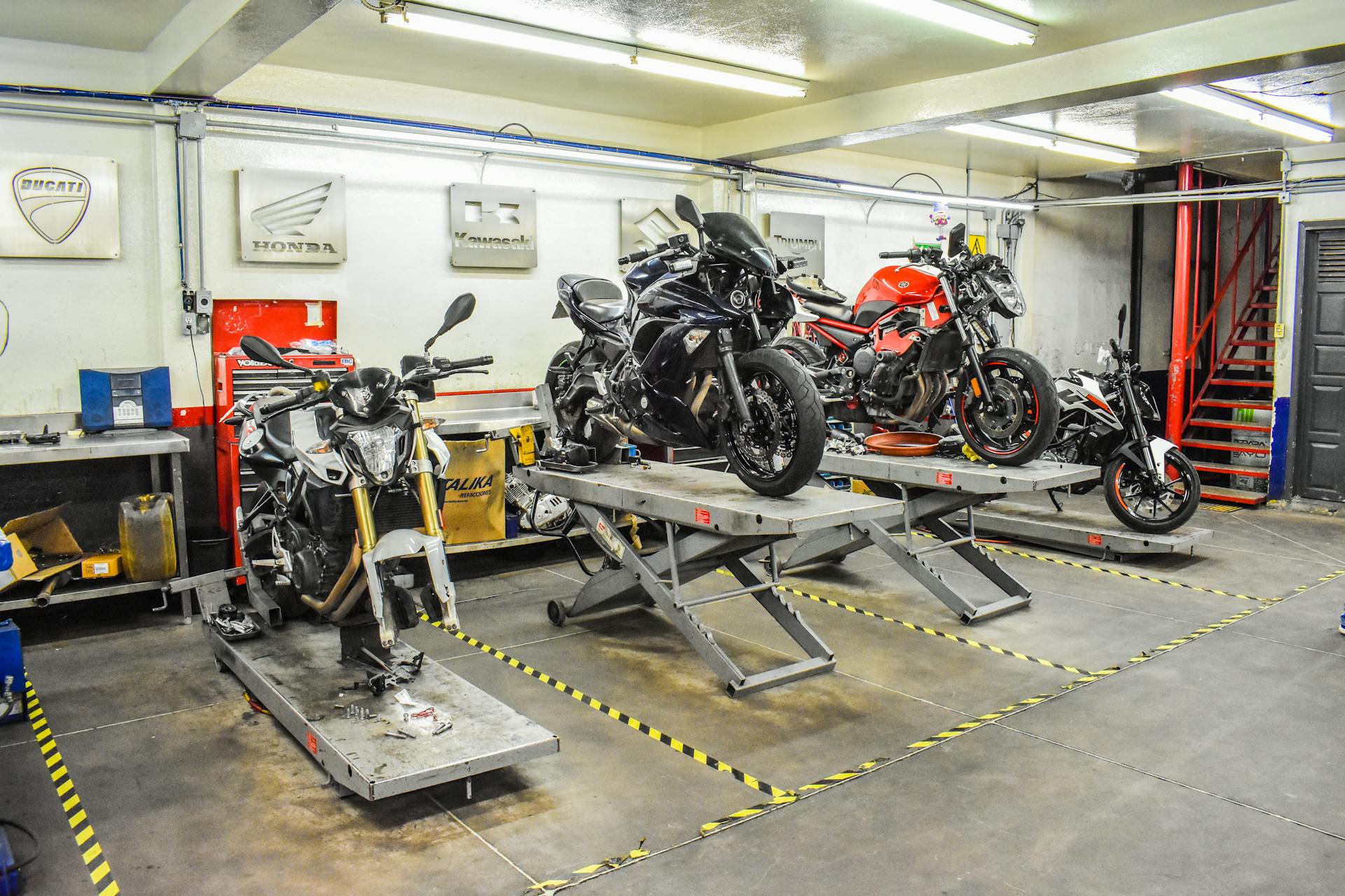 Motorcycle repair shop featuring Ducati, Honda, and Kawasaki bikes on stands.