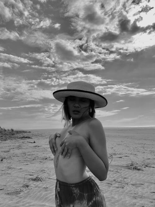 Free Black and white of nude female in hat covering breast and standing on sandy beach in sunny day Stock Photo