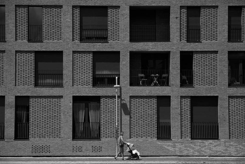 A woman pushing a stroller past a modern building facade in Paris.
