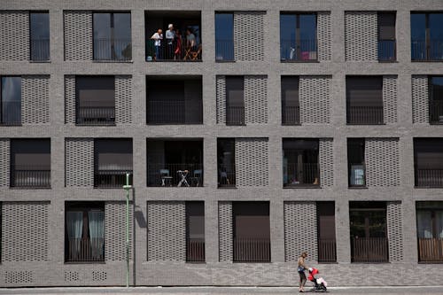 A Woman with a Stroller Walking by a Gray Building