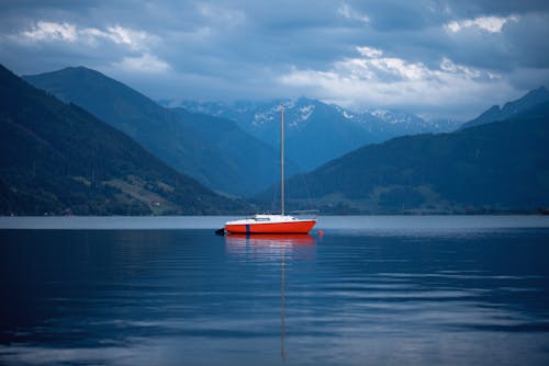 白い雲と青い空の下の山の近くの海の赤と白のボート