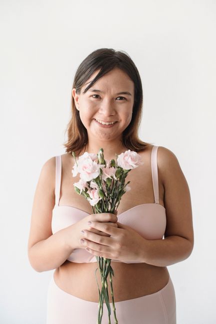 A woman in lingerie smiles while holding pink flowers, exuding joy.