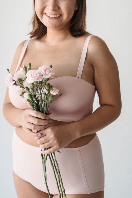 Smiling woman in underwear holding pink carnations against a white background.