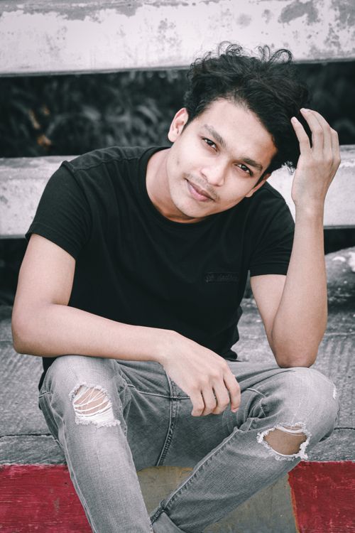 Free Young man with stylish ripped jeans sitting outdoors, exuding confidence and casual style. Stock Photo