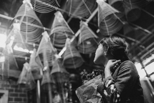 Unrecognizable Asian pilgrim contemplating incense coils in Buddhist church