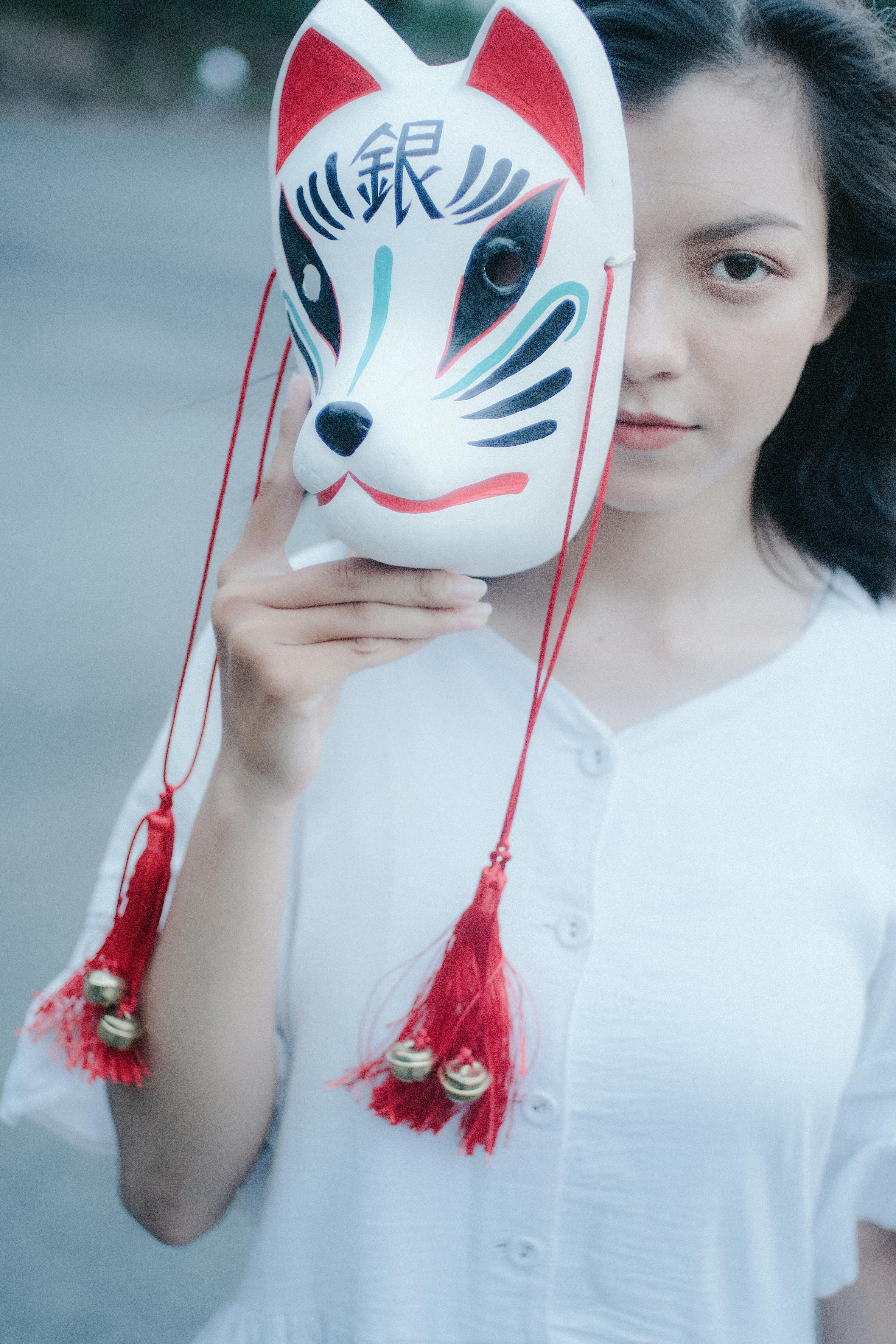年轻女子在户外用装饰性狐狸面具半遮着脸