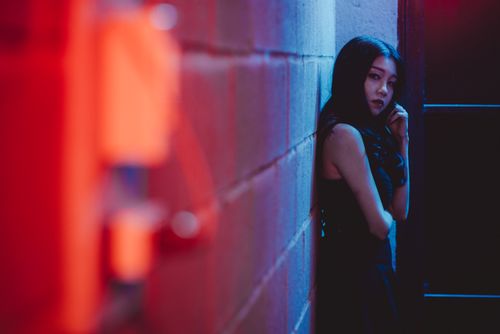 Free Side view of young contemplative ethnic female in trendy apparel looking at camera near wall illuminated by artificial light Stock Photo