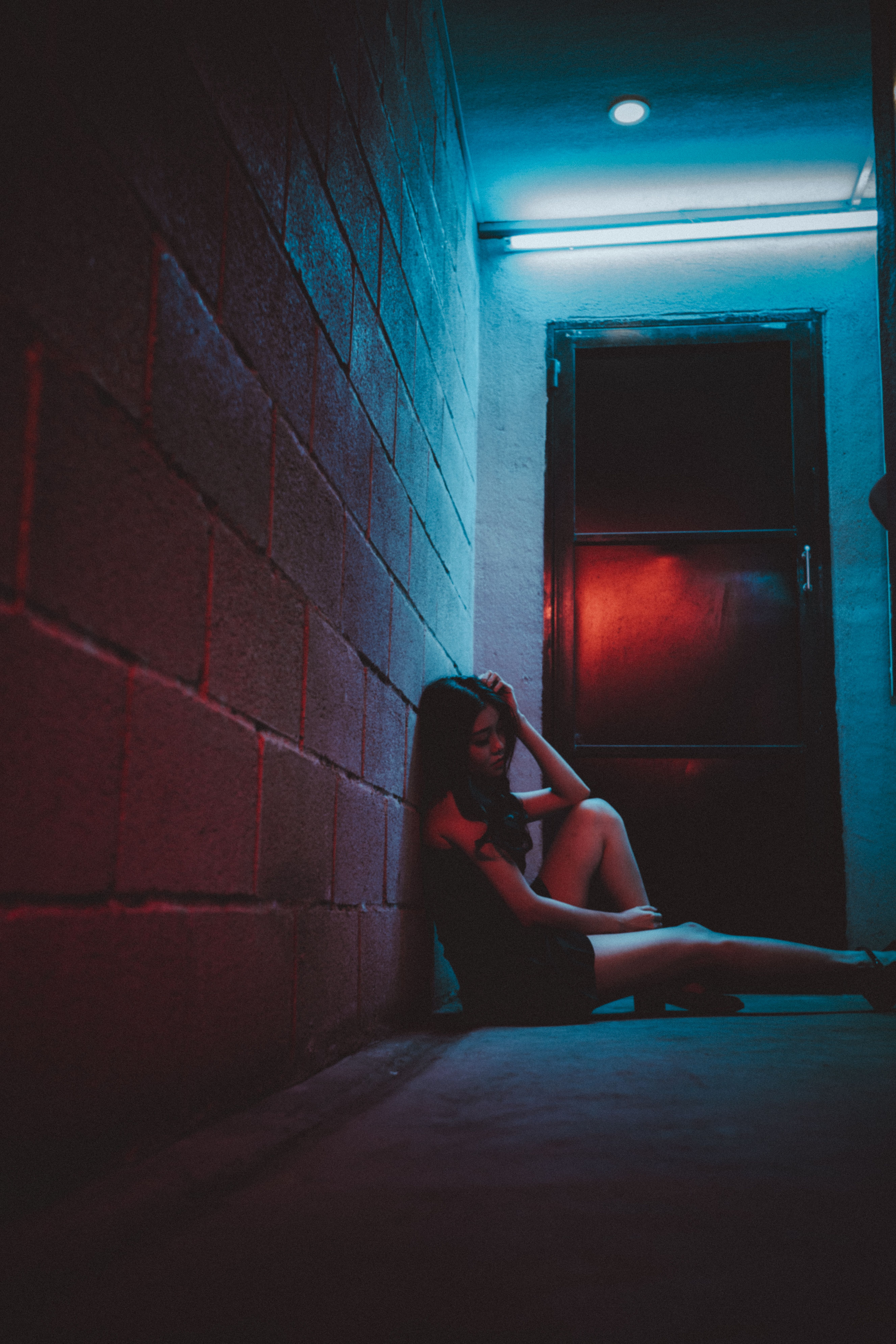 黄昏时分，一名身穿时尚服装的匿名女性低角度侧身坐在石墙边的地板上，手触头部
