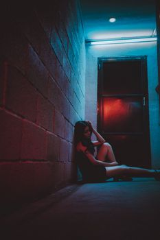 黄昏时分，一名身穿时尚服装的匿名女性低角度侧身坐在石墙边的地板上，手触头部
