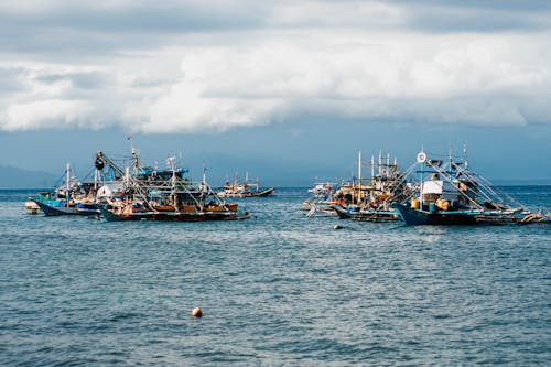 Fishing boats floating on rippled blue water of sea in overcast cloudy day