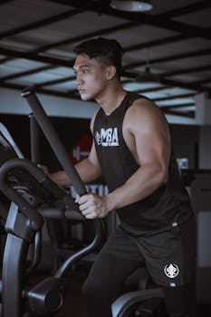 Side view of determined male in sportswear with biceps exercising on ellipsoid machine in gym during cardio workout in daytime