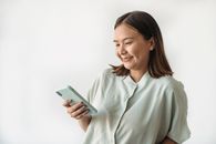 一位穿着休闲装的快乐女人在白色背景下微笑着使用智能手机