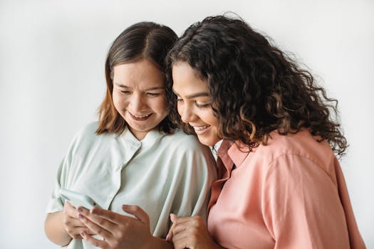 Two women smiling while looking at a smartphone, depicting happiness and friendship.