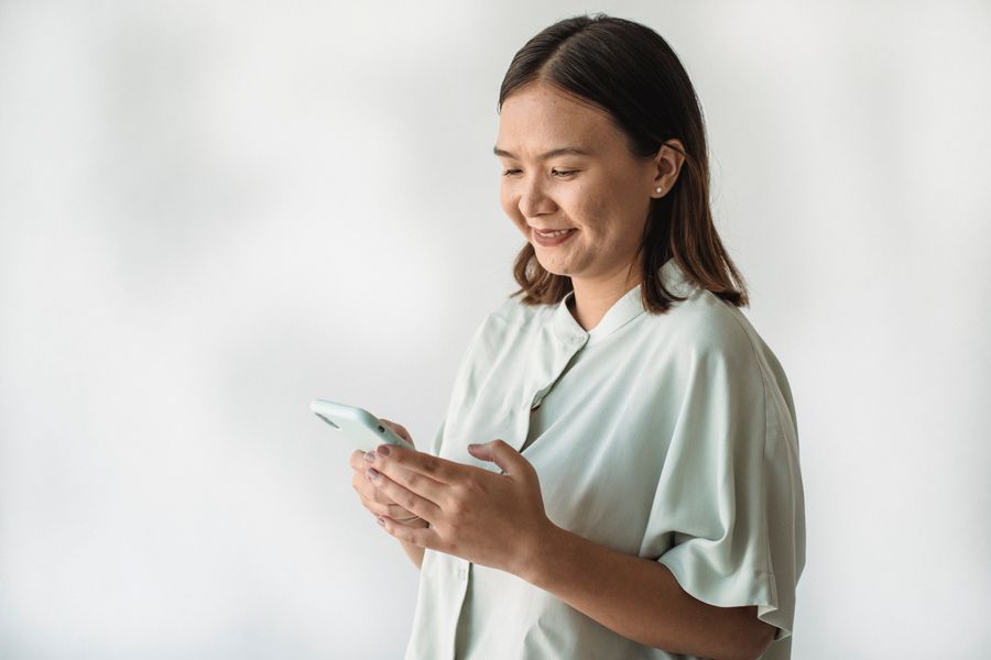 A woman in a mint shirt smiles as she reads a text on her phone