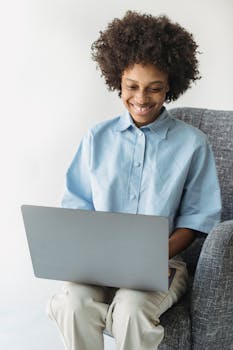 Young woman with afro hairstyle smiling while using a laptop indoors.