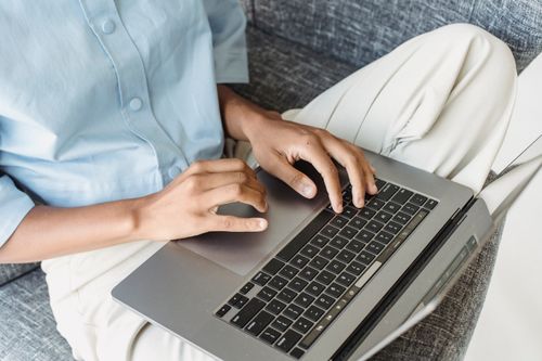 Free Close-up of a person typing on a laptop in a casual work setup indoors. Stock Photo