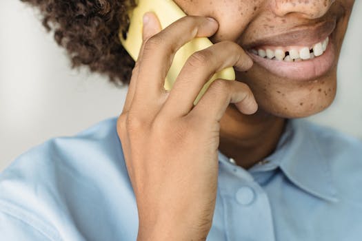 Close-up of an adult holding a yellow phone while smiling, showcasing natural freckles.