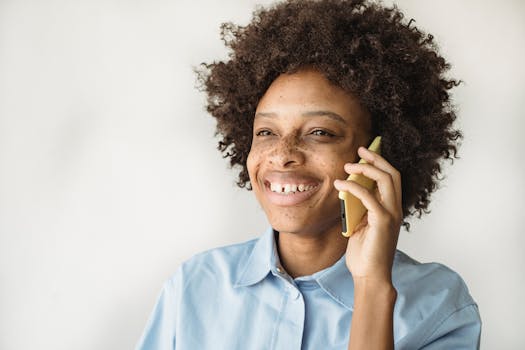 Happy woman with curly hair smiling while talking on phone against white background
