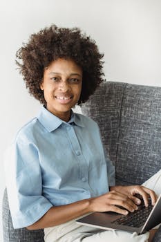 Smiling woman sitting on couch using a laptop, capturing a relaxed work-from-home moment.