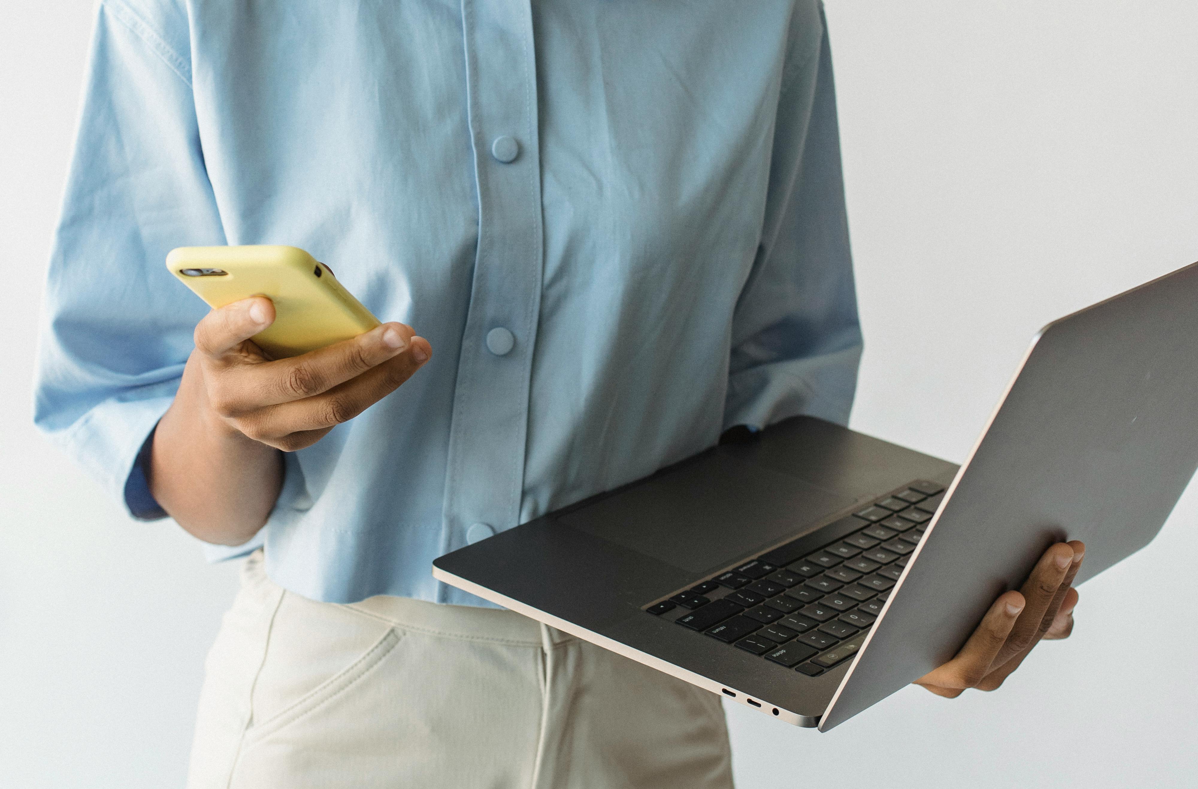 Close-up of a person multitasking with a laptop and smartphone, emphasizing technology use.