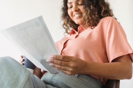 A woman smiles while reading a document and holding a coffee cup indoors.