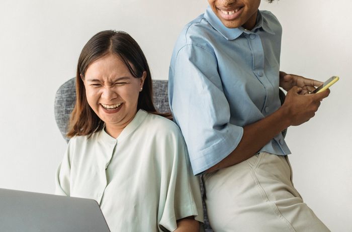 Two colleagues laughing together at a laptop — photo by Antonius Ferret on Pexels