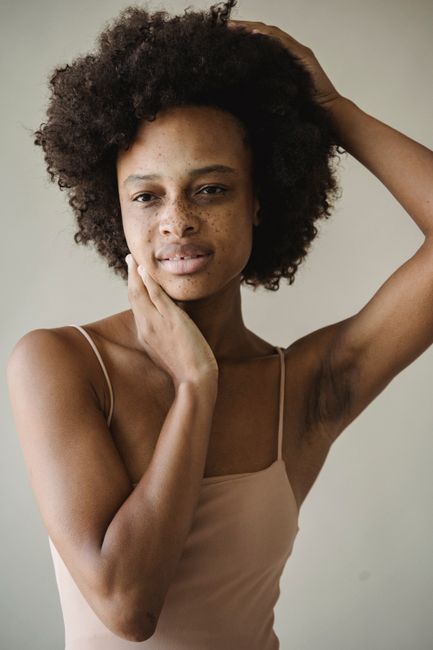 Portrait of a young woman with afro hairstyle and freckles in a nude tank top.