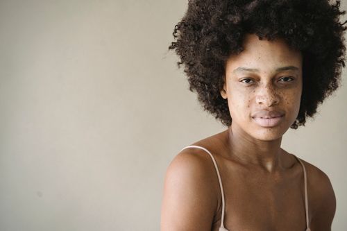 Free Close-up portrait of a woman with natural afro hair and freckles wearing a spaghetti strap top. Stock Photo